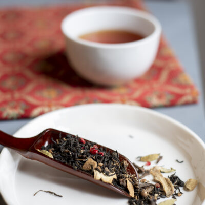 Foglie di tè chai in un cucchiaio di legno e sullo sfondo una ciotola di tè