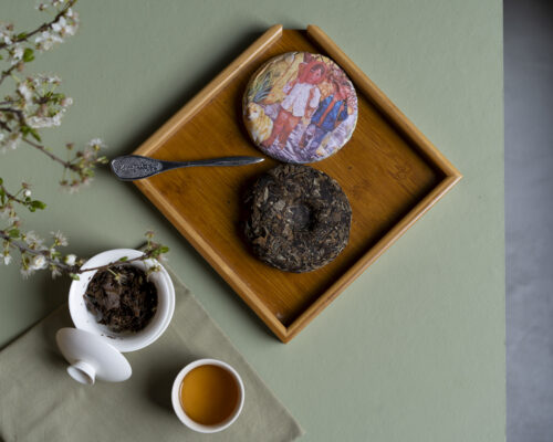 Un disco avvolto nella carta, un disco aperto, un ramo fiorito, una gaiwan aperta e una tazzina con il tè