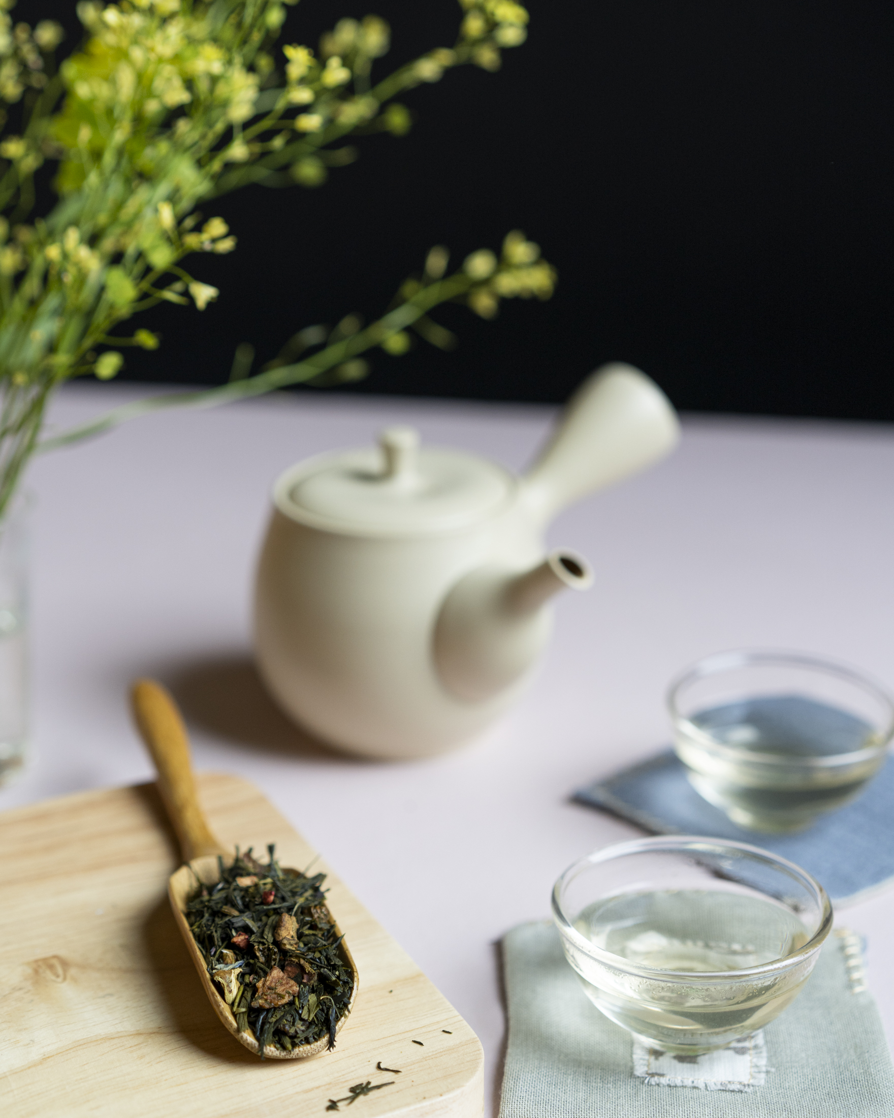 Foglie di tè, sullo sfondo fiori, una kyusu e due tazzine