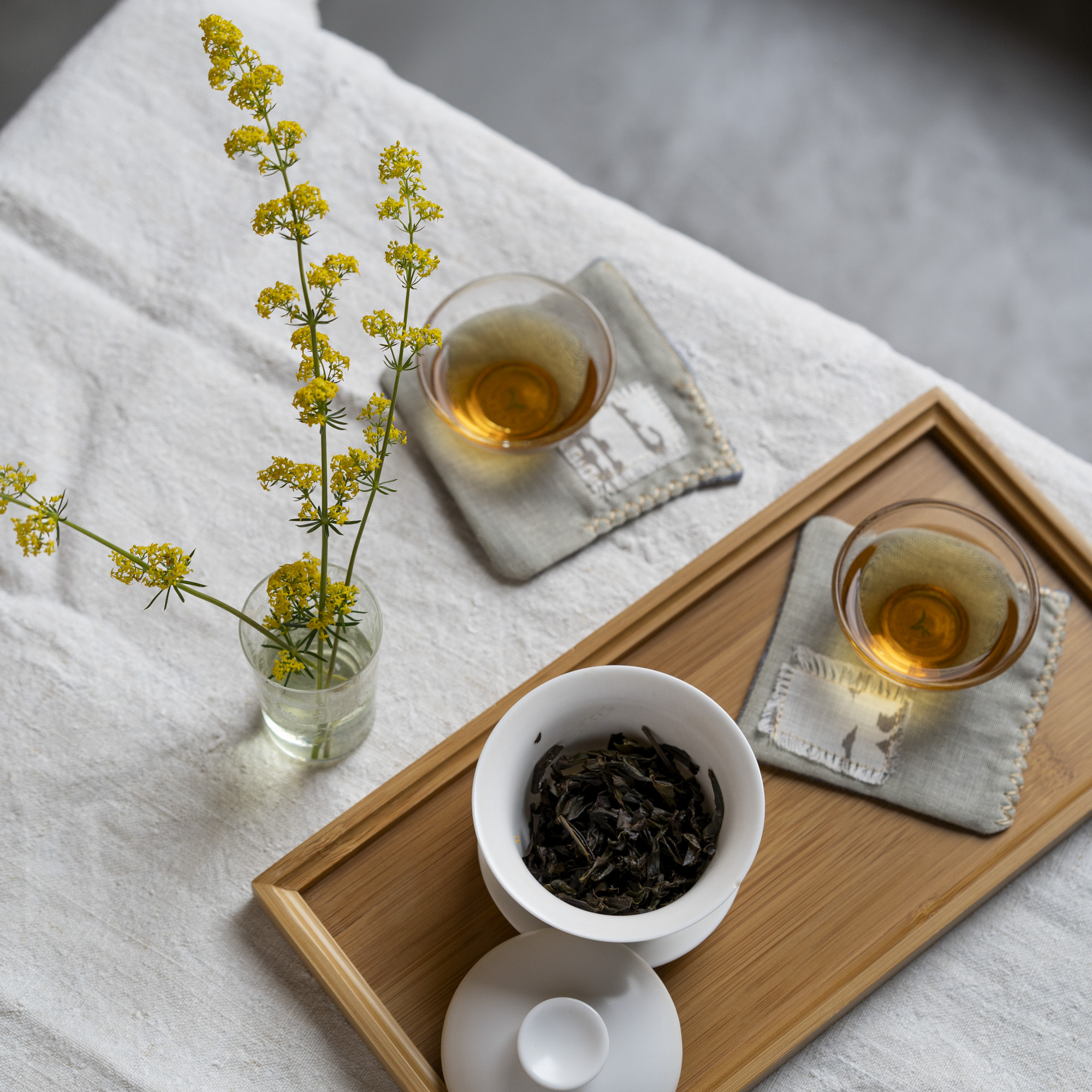 Gaiwan con foglie infuse, due tazzine di tè, fiori gialli
