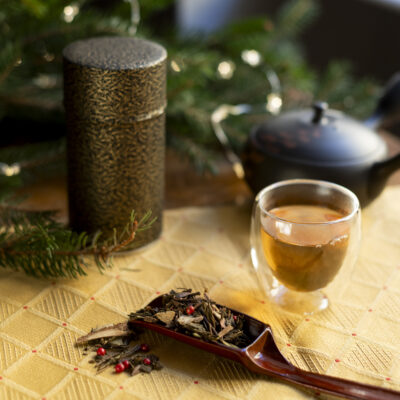 Una tazza di tè, un cucchiaio di legno con foglie di tè, sullo sfondo una kyusu nera e una scatola portatè con decori dorati