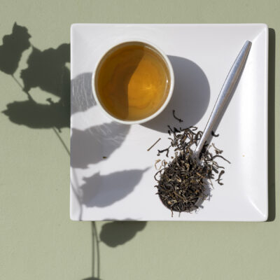 Una tazza di tè, un cucchiaio di foglie di tè e l'ombra di un ramo di glicine