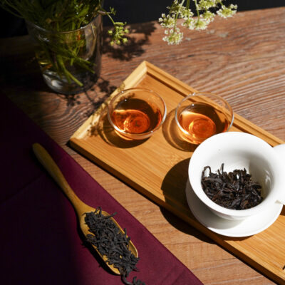 Gaiwan aperta, due tazzine di tè e foglie asciutte in un cucchiaio di legno