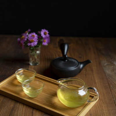 Una brocca di tè caldo con due tazzine colme, sullo sfondo un mazzolino di Aster e una teiera nera