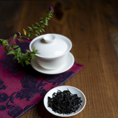 Foglie di tè asciutte, sullo sfondo un rametto verde e una gaiwan chiusa