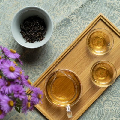 Due tazzine e una brocca di tè, una gaiwan aperta con le foglie bagnate e un mazzolino di settembrini viola.