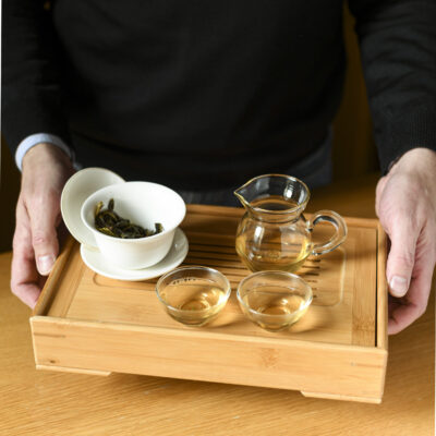 Un tavolino da tè con la gaiwan aperta dove si vedono le foglie infuse, una brocca e due tazzine di tè